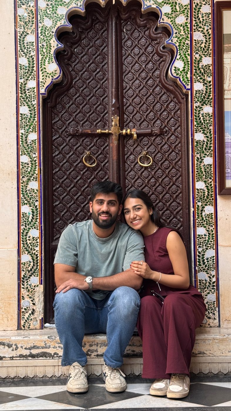 Aman and Ashmeet sitting together on the step of a carved palace doorway